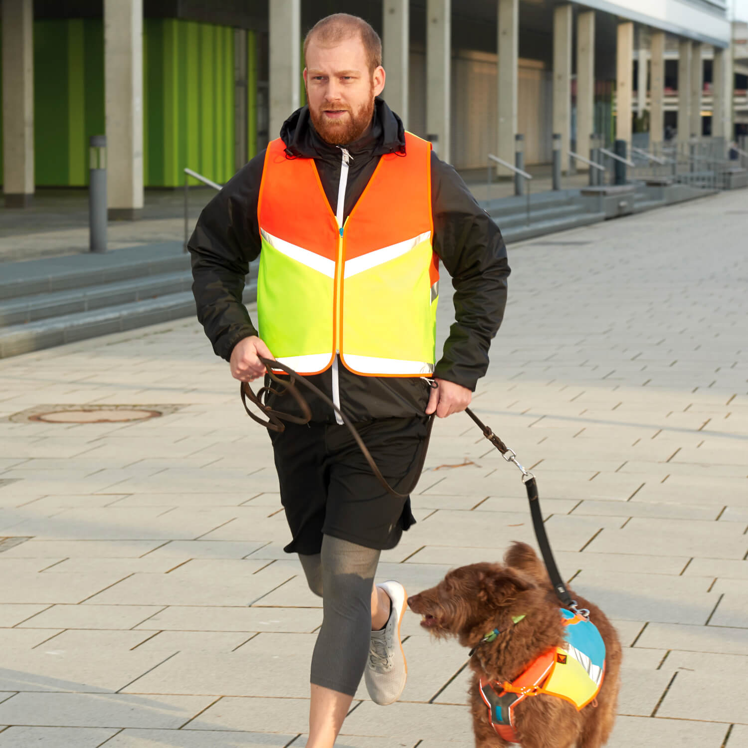 Jogger mit rot gelber Warnweste mit Hund in blau gelber Warnweste an der Leine